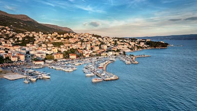 Un pueblo costero con un puerto deportivo lleno de barcos, rodeado de colinas y un cielo despejado.