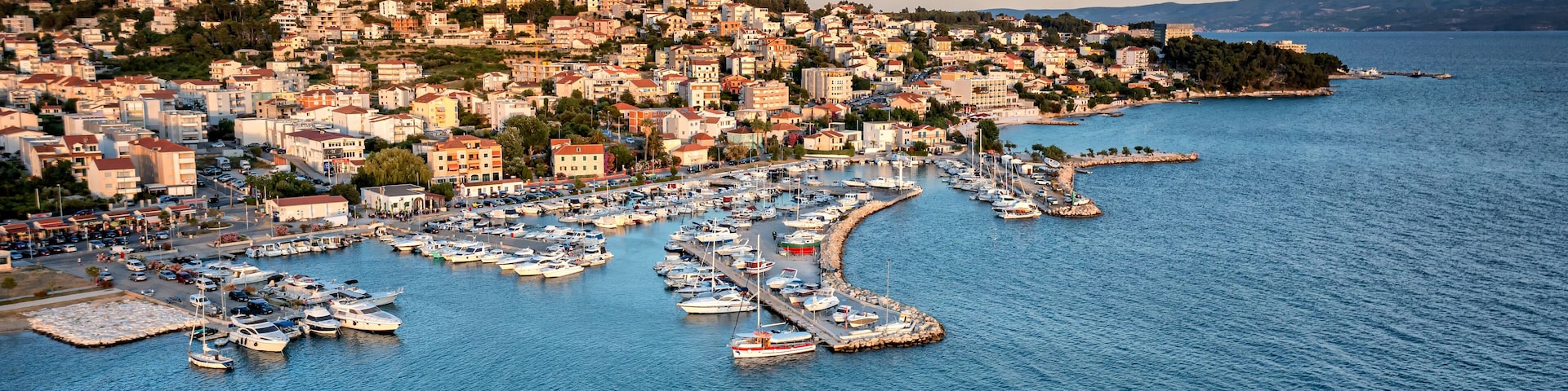 Un pueblo costero con un puerto deportivo lleno de barcos, rodeado de colinas y un cielo despejado.