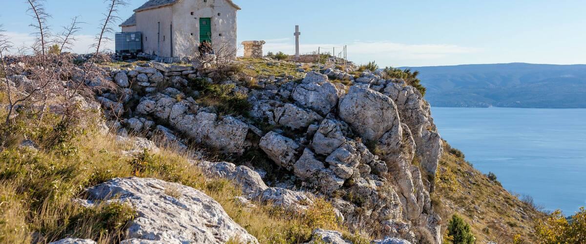 A white church with a bell tower on a rocky cliff overlooking a body of water.