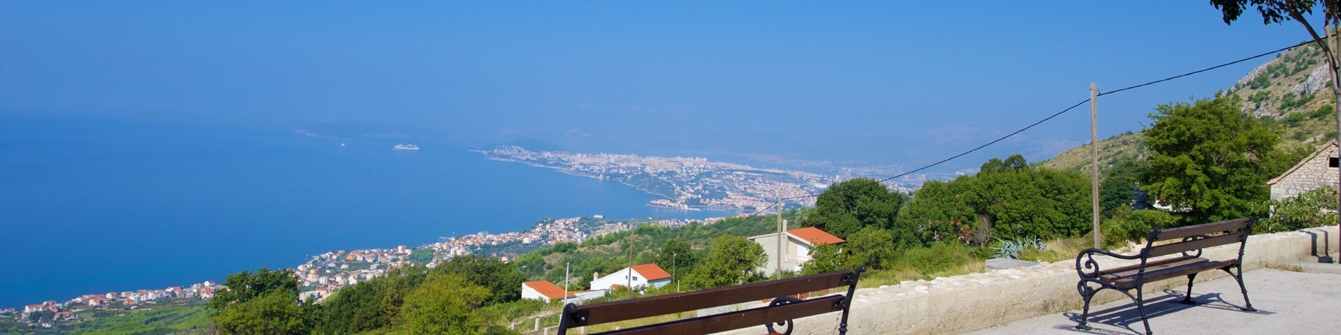 A coastal view with two benches overlooking a town and the sea.