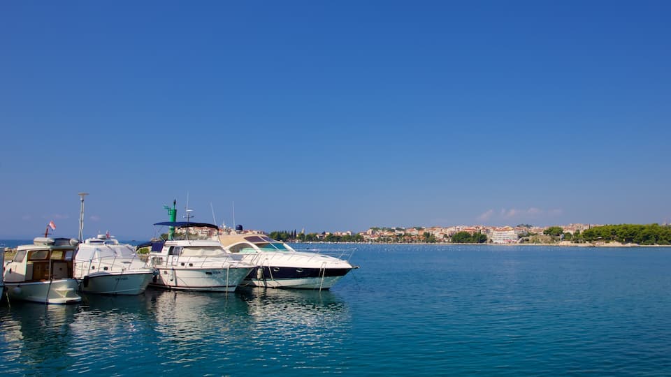A marina with several boats docked, a clear blue sky, and a coastal town in the background.
