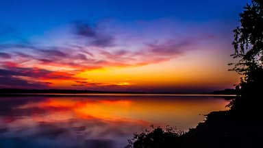 A sunset over a calm lake with vibrant colors reflected on the water.