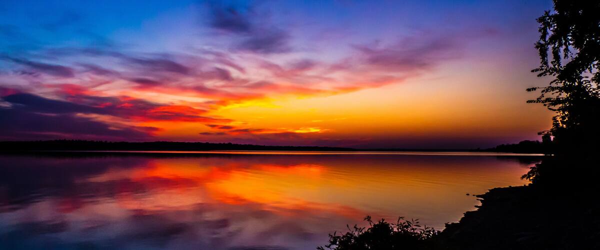 A sunset over a calm lake with vibrant colors reflected on the water.