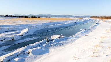 Um rio congelado com margens cobertas de neve e montanhas ao longe.