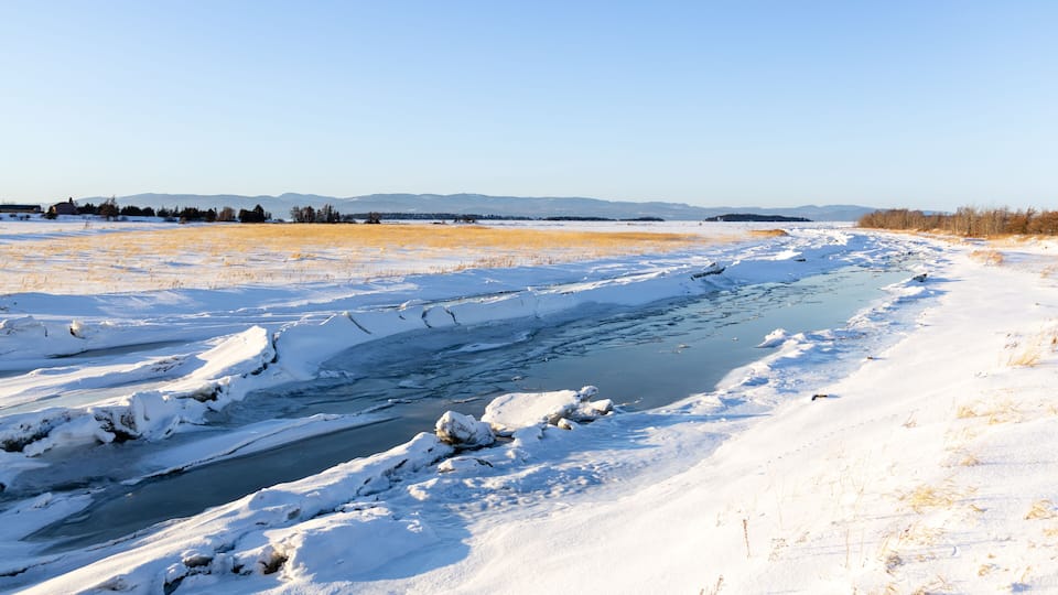 A frozen river with snow-covered banks and distant mountains.