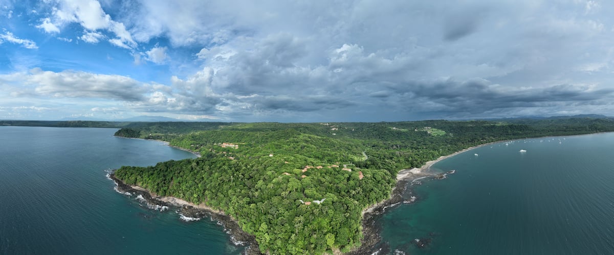 An aerial view of a lush, green island surrounded by calm waters, with a clear sky above.