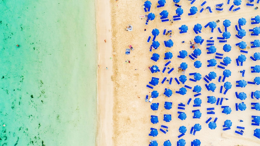 A beach with turquoise water and numerous blue umbrellas.