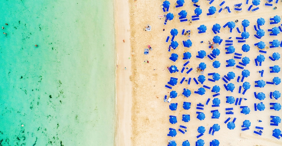 Una playa con agua turquesa y numerosas sombrillas azules.