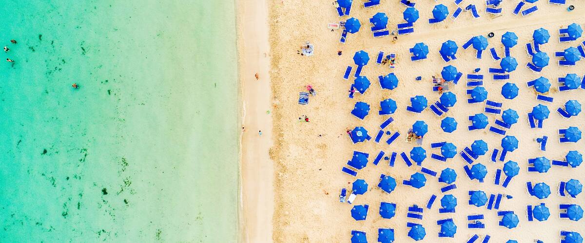 A beach with turquoise water and numerous blue umbrellas.