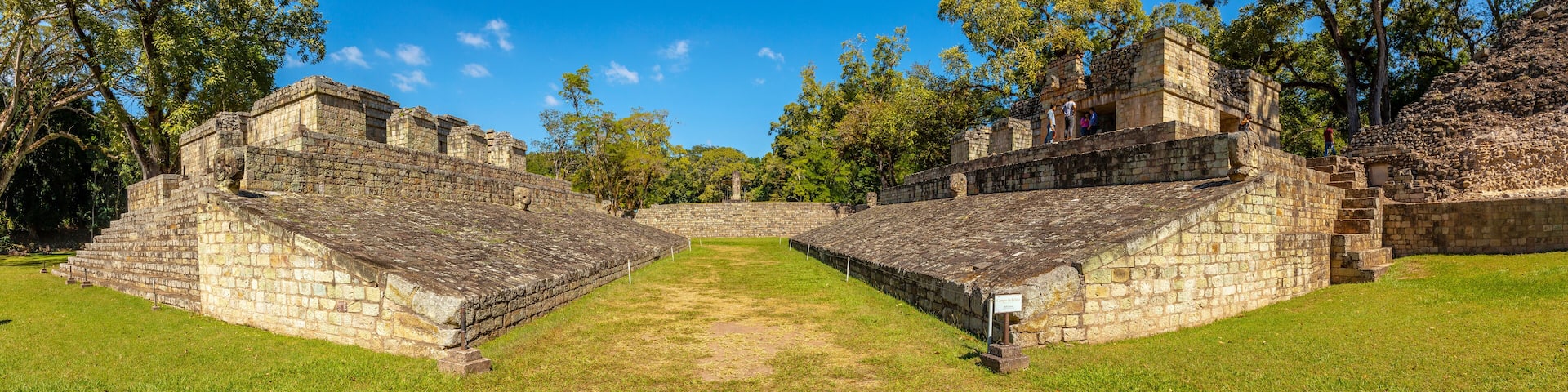 Ancient stone structures with a central open space surrounded by trees.