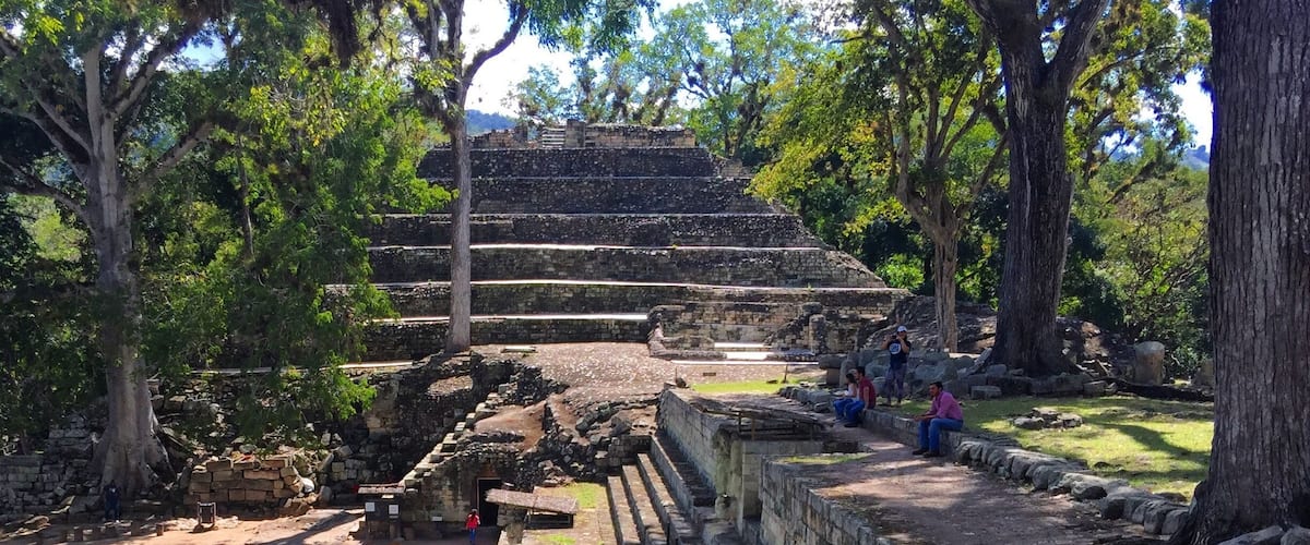 Ancient stone steps leading up to a pyramid-like structure surrounded by trees.