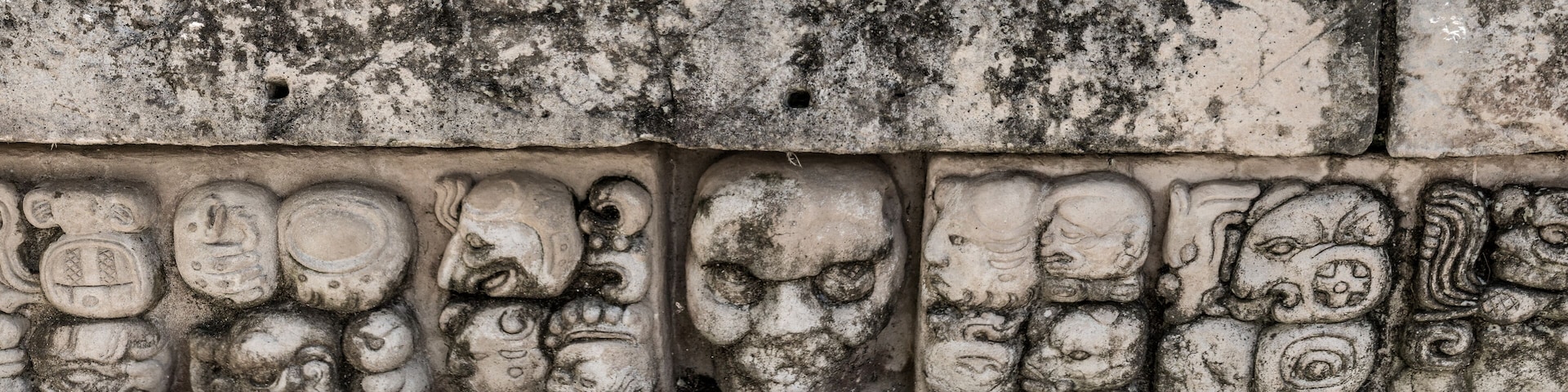Una pared de piedra erosionada con antiguas tallas de rostros y símbolos.
