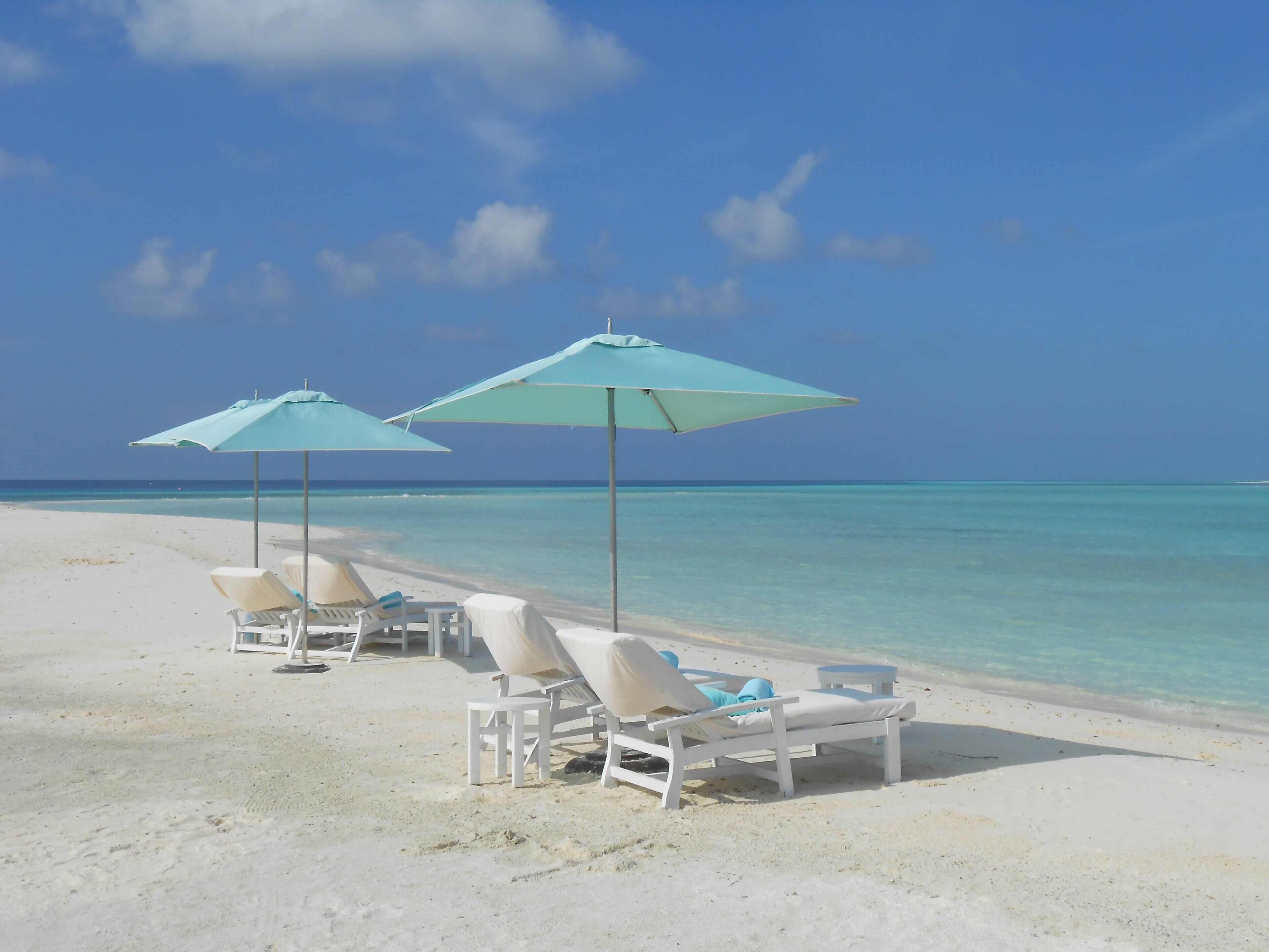 A beach with white lounge chairs and turquoise umbrellas.