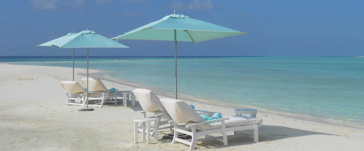 A beach with white lounge chairs and turquoise umbrellas.