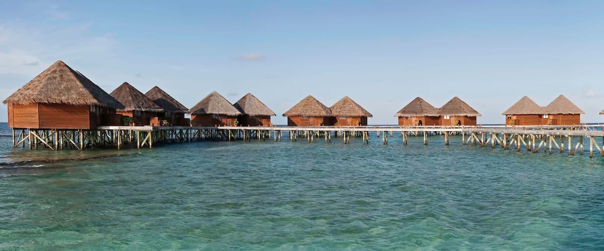 Overwater bungalows connected by a wooden pier over turquoise water.