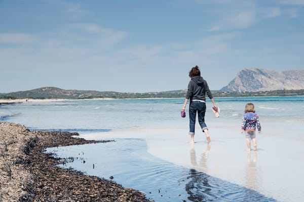 Una spiaggia con costa rocciosa, acqua calma e montagne sullo sfondo.