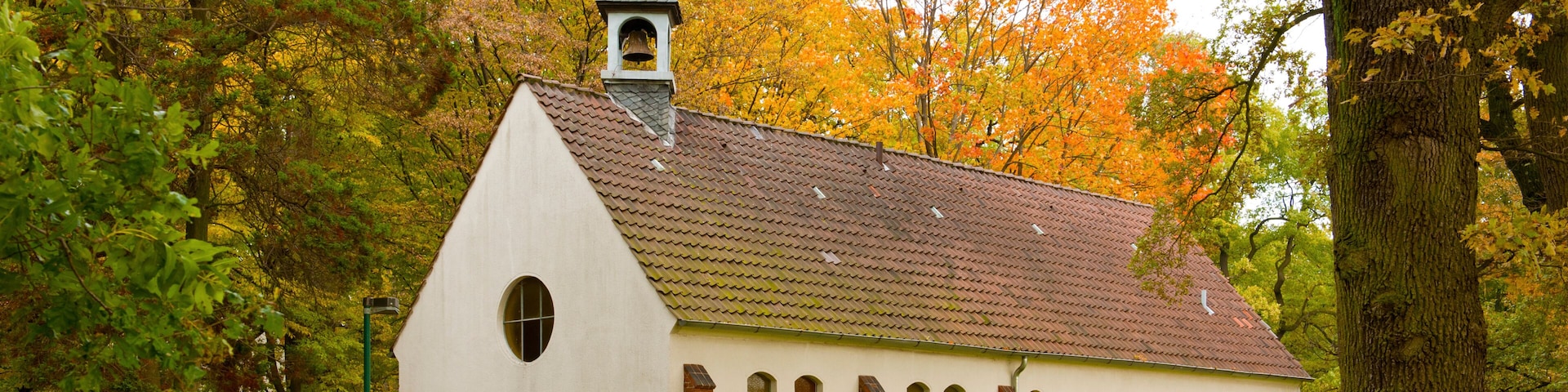 Uma igreja branca com um campanário, rodeada por árvores em tons de outono.