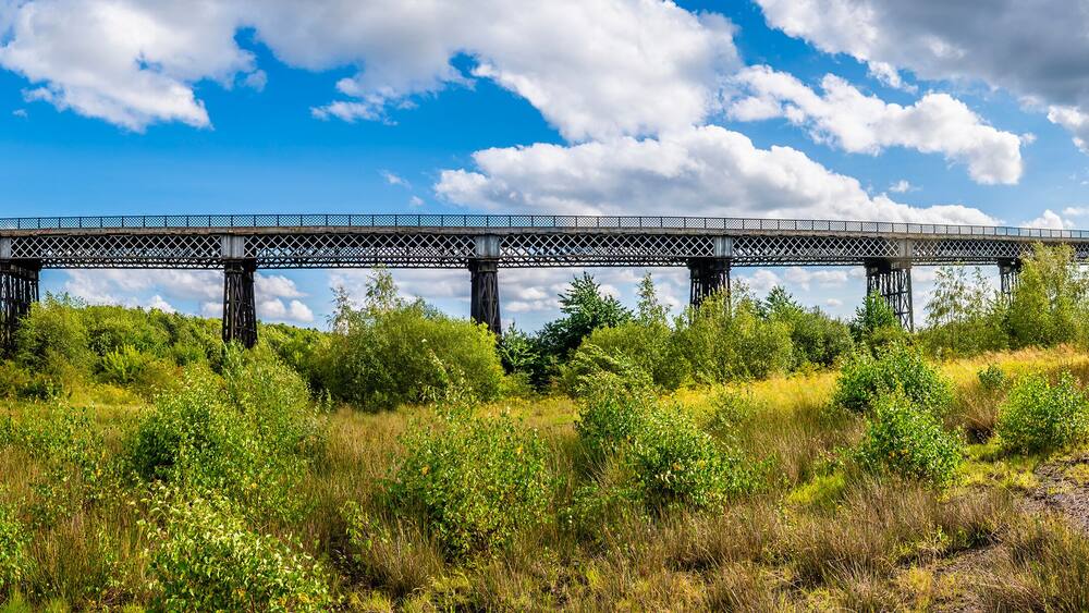 Un pont enjambant une rivière, avec une végétation luxuriante et un ciel dégagé.