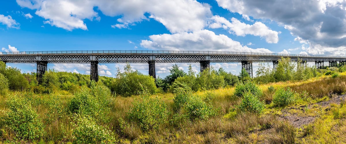A bridge over a river with lush greenery and a clear sky.