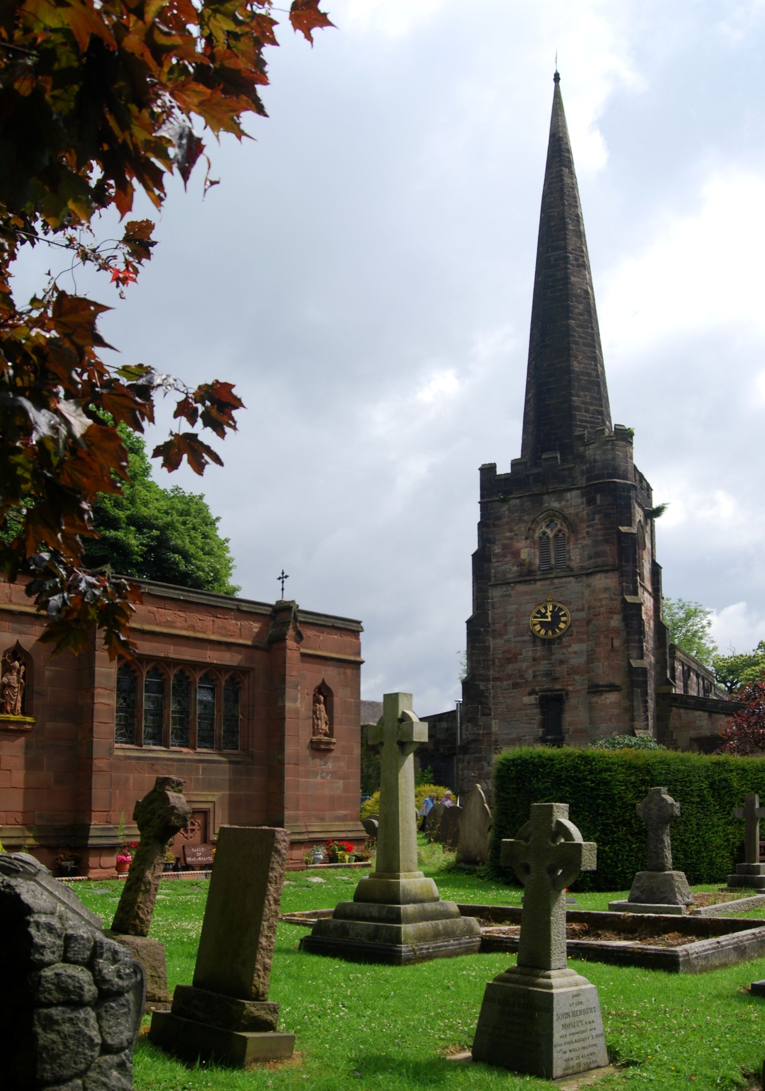 A church with a tall spire, stone crosses, and a cemetery.