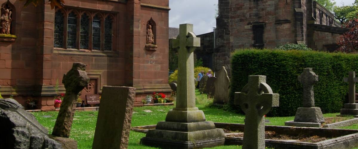 A church with a tall spire, stone crosses, and a cemetery.