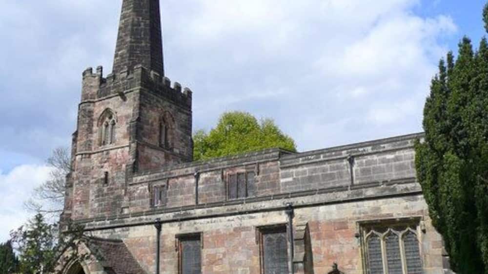 A historic church with a tall spire, stone walls, and a graveyard.