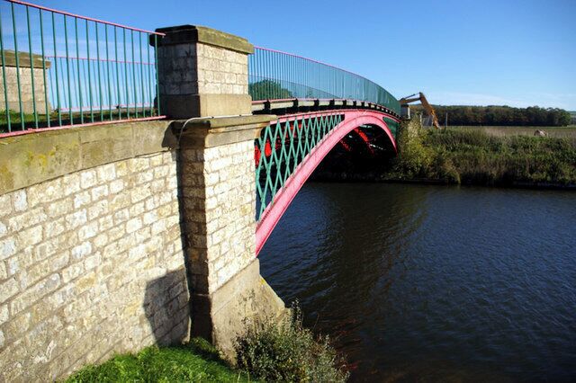 A stone bridge with a pink arch over a river.