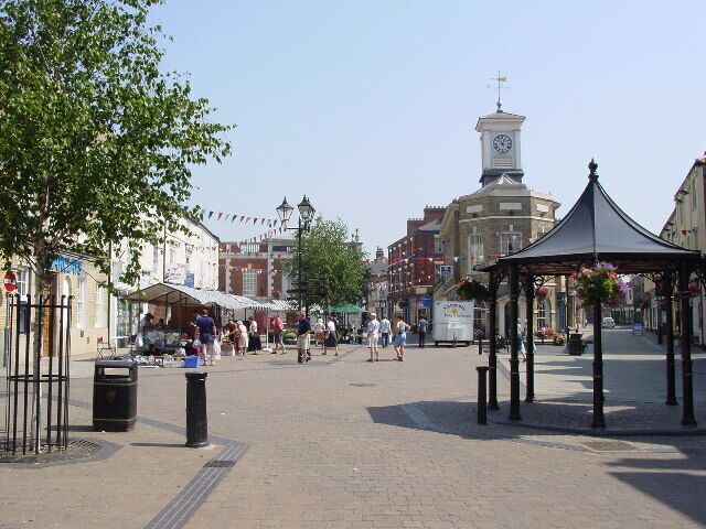 A town square with a clock tower, market stalls, and a gazebo.