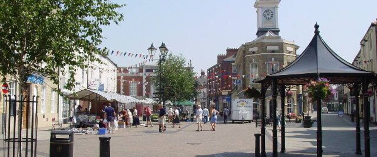 A town square with a clock tower, market stalls, and a gazebo.