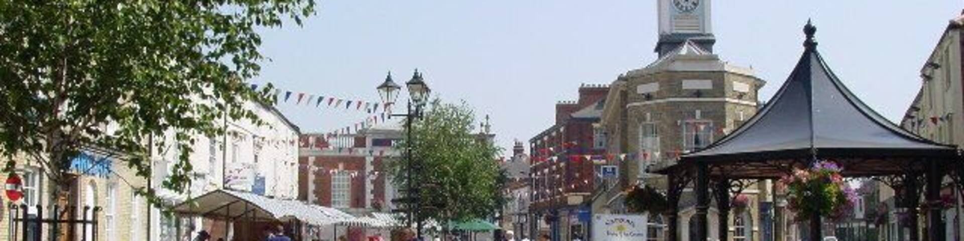 A town square with a clock tower, market stalls, and a gazebo.