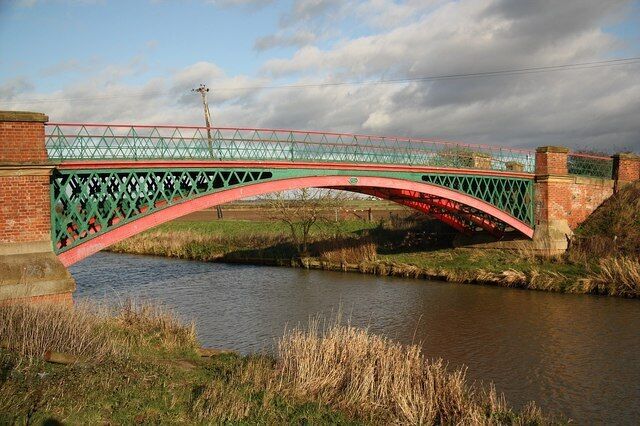 A red and green bridge over a river with brick walls on either side.