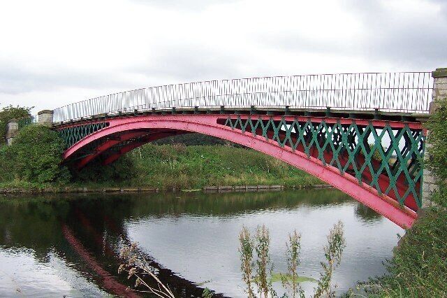 A red arched bridge over a calm river with greenery on either side.