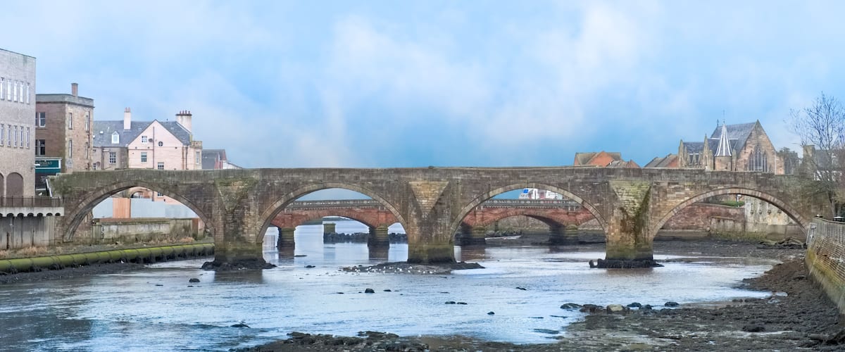 A stone bridge over a river with buildings in the background.