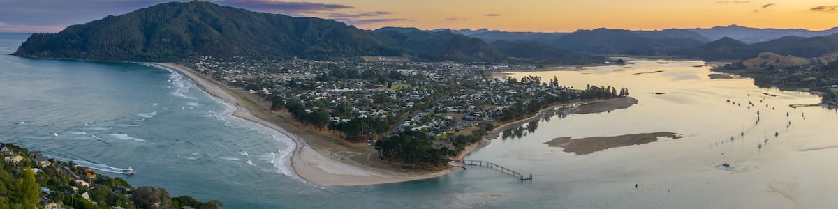 A coastal town with a beach, a pier, and mountains in the background.