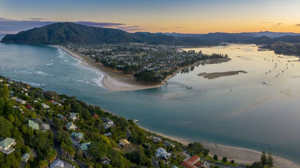 A coastal town with a beach, a pier, and mountains in the background.