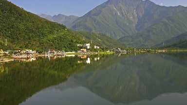 A calm lake reflecting mountains and a small town with buildings along the shore.