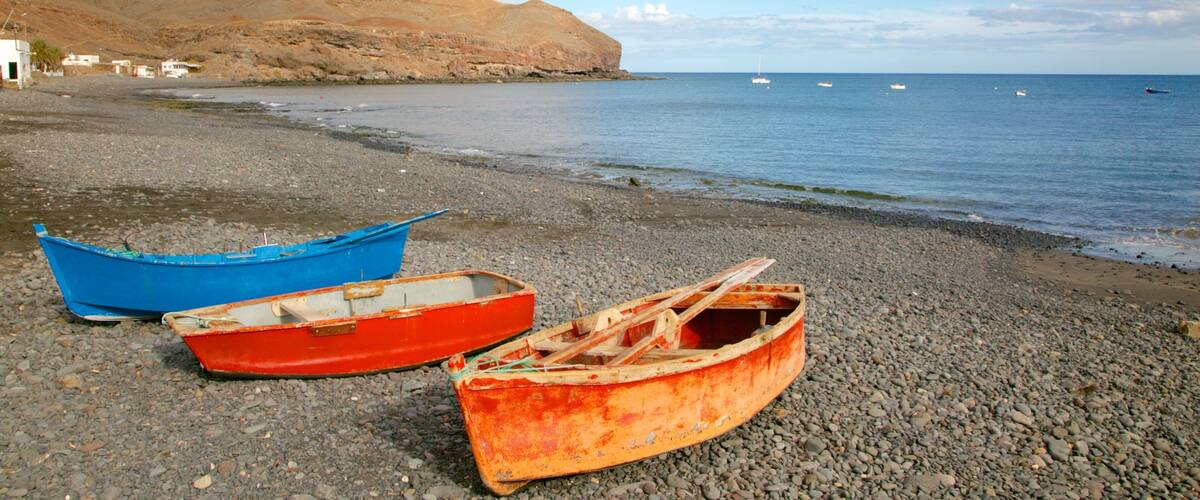 Two boats on a pebbly beach with a rocky hill in the background and calm sea.