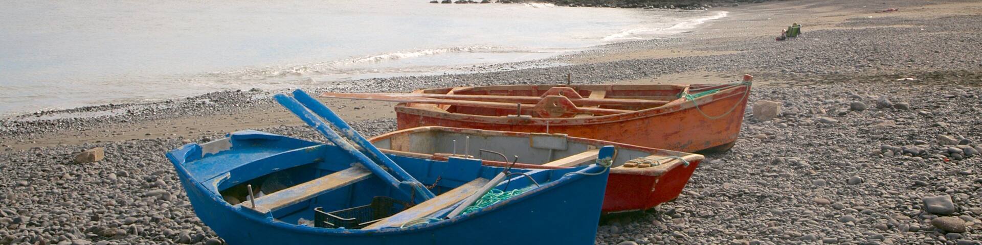 A rocky beach with two boats, one blue and one orange, and a distant building on a cliff.