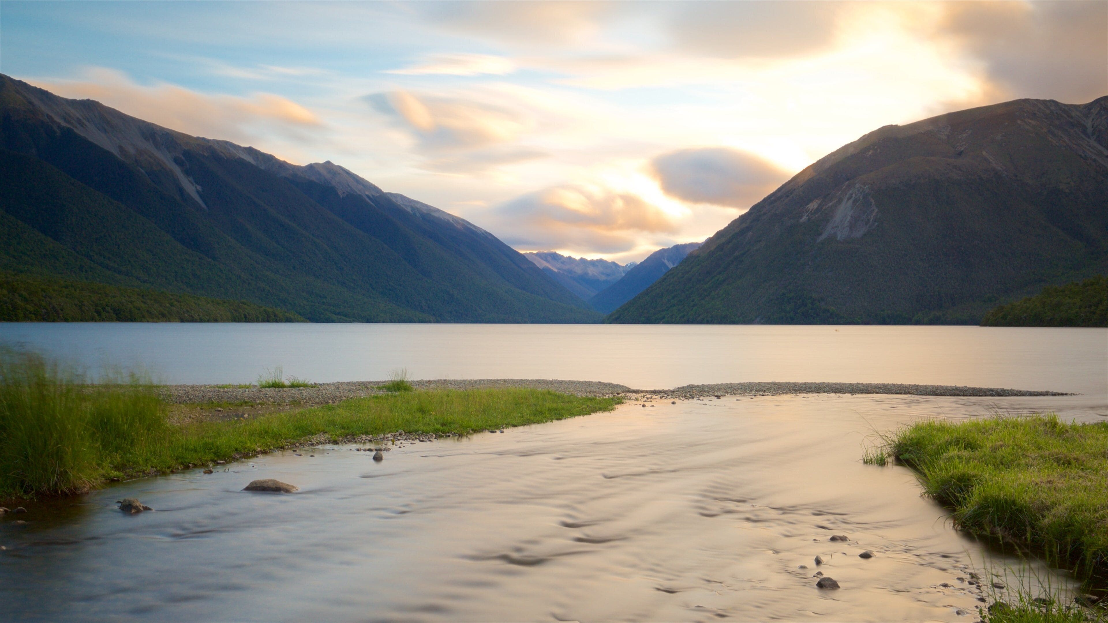 A calm river flowing through a valley with mountains on either side.
