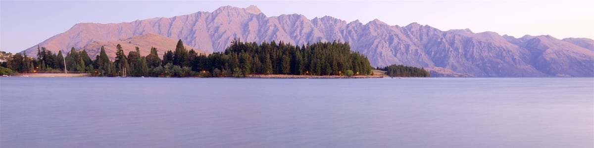 A calm lake with rocky shores and a mountain range in the background.