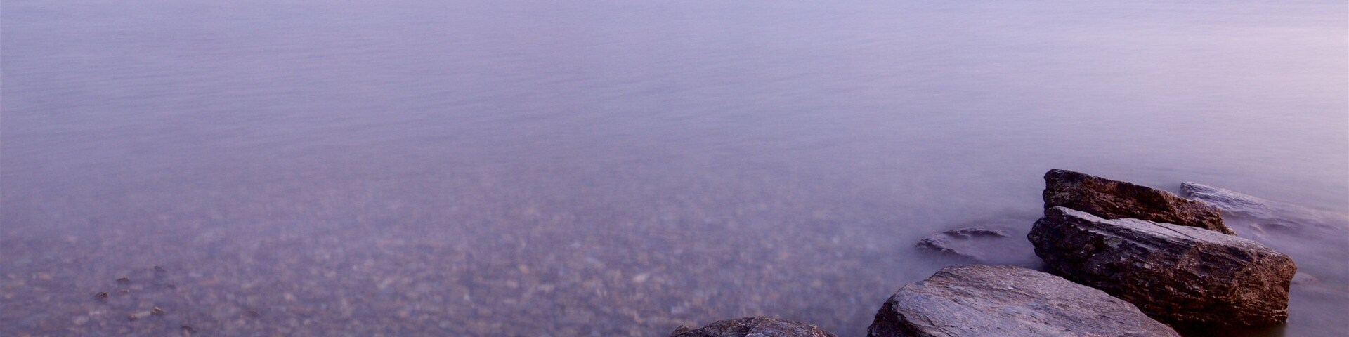 Um lago calmo com margens rochosas e uma cadeia de montanhas ao fundo.