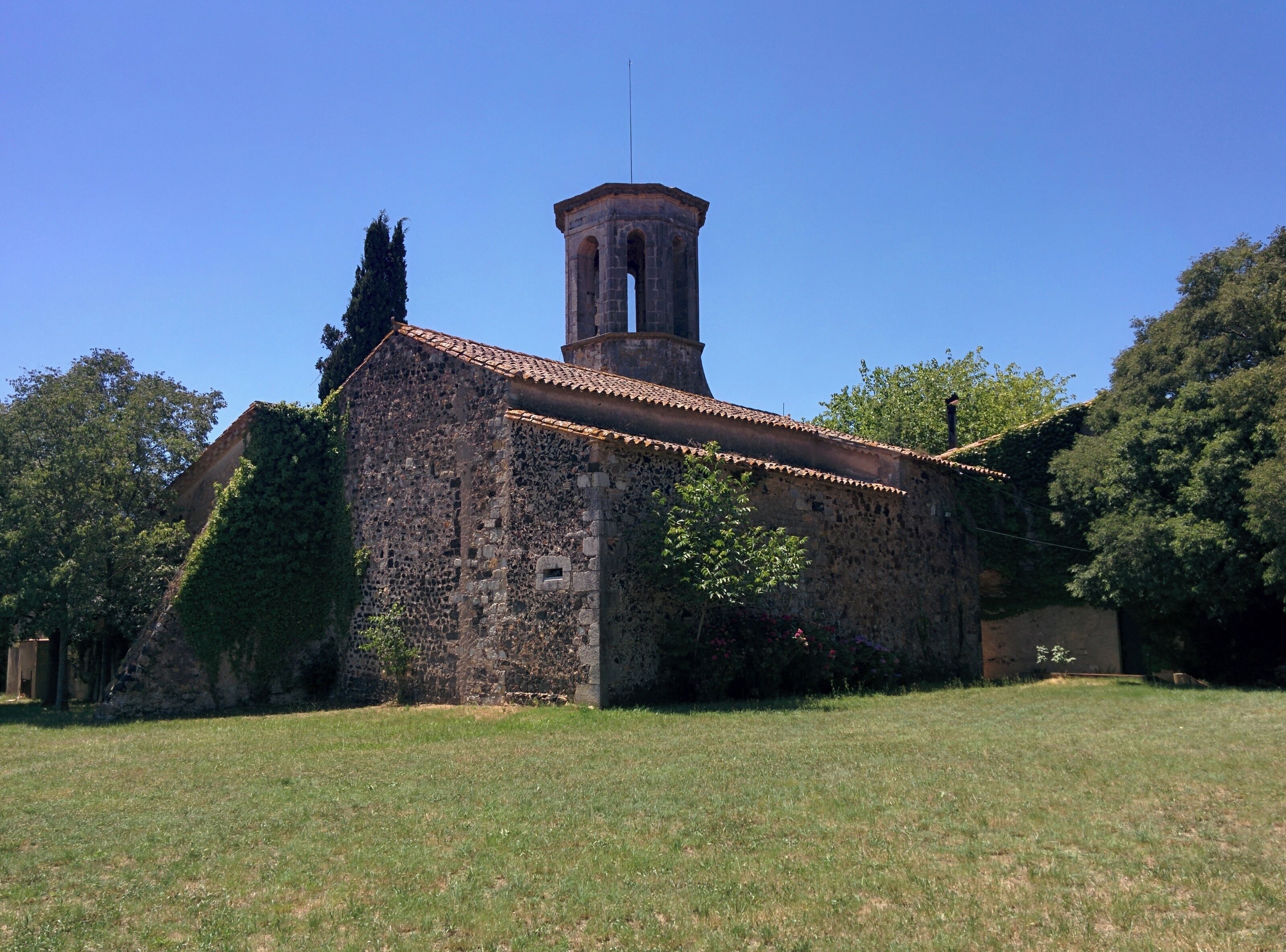 An old stone church with a bell tower, surrounded by trees and grass.