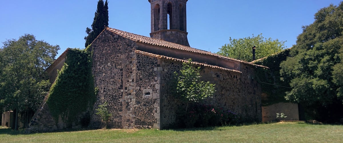 An old stone church with a bell tower, surrounded by trees and grass.