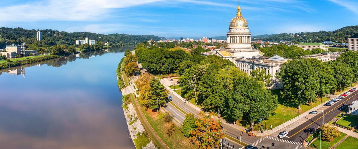 A river with a cityscape, a prominent golden-domed building, and lush green trees.