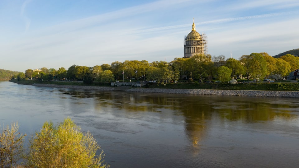 A river with a large building on a hill, surrounded by trees and a few houses.