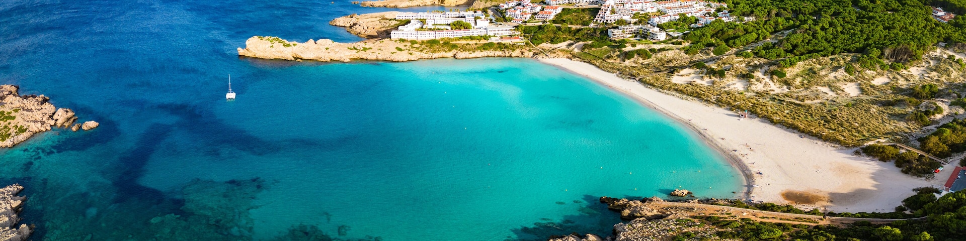 A coastal town with a beach, clear turquoise waters, and a rocky coastline.