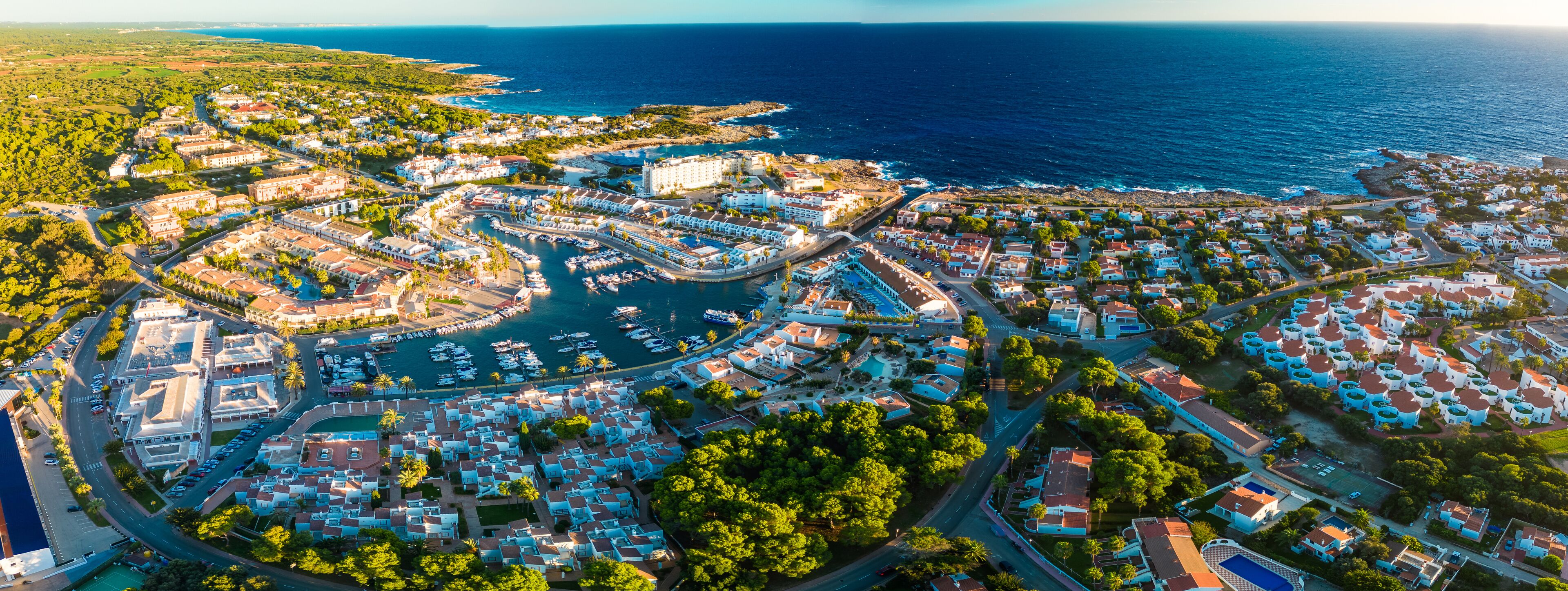 An aerial view of a coastal town with a marina, residential buildings, and a coastline.