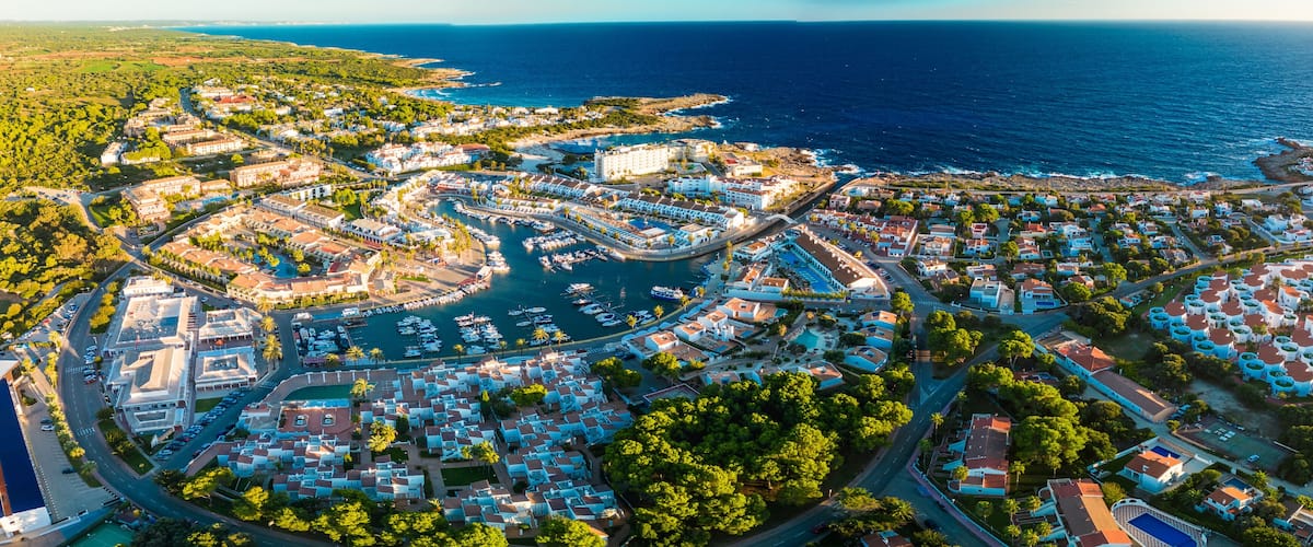 An aerial view of a coastal town with a marina, residential buildings, and a coastline.