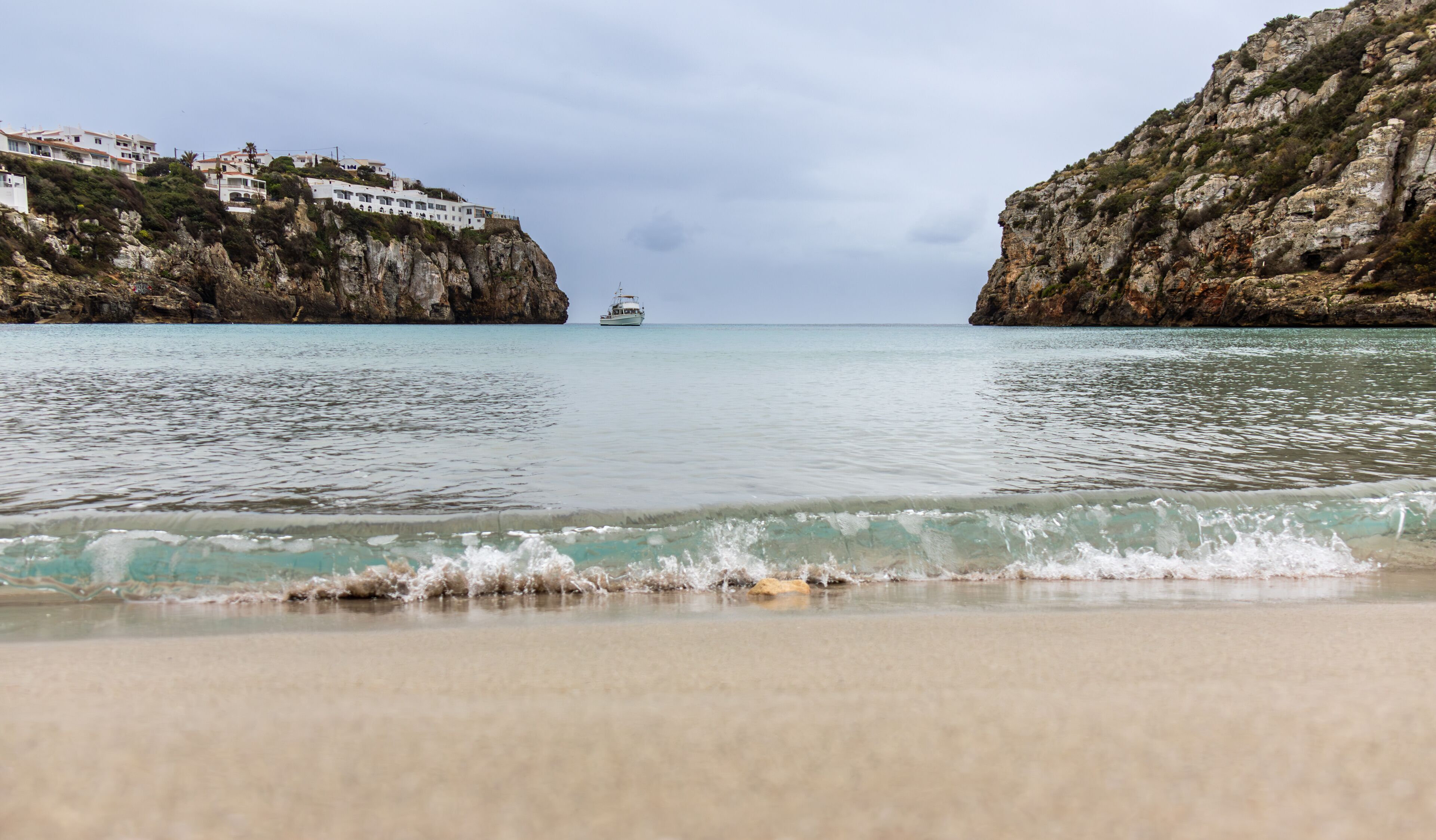 Cala en Porter, a hidden gem on the island of Menorca. Golden sand beach embraced by crystal clear turquoise waters. The rocky cliffs create a spectacular contrast with the blue sea and  sky. Spain