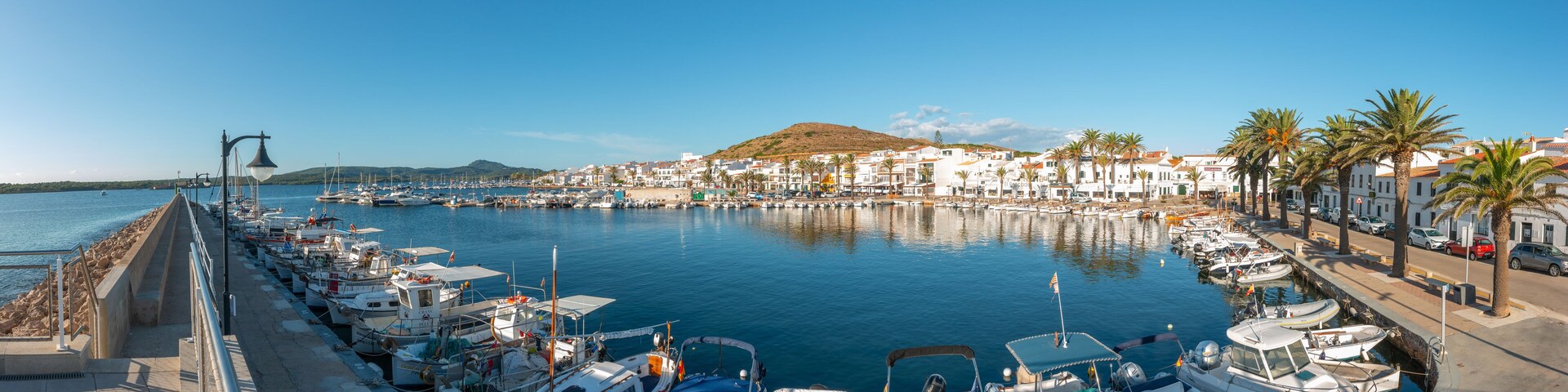 Un puerto deportivo con barcos amarrados a lo largo de la costa, rodeado de edificios blancos y palmeras.